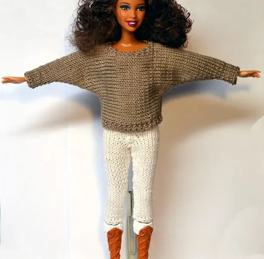 Barbie i beige stickad oversize-tröja med vida ärmar och vita byxor.