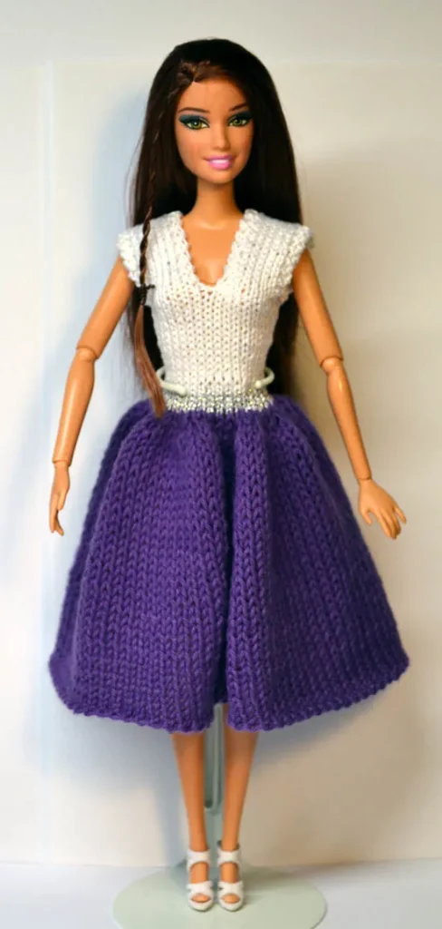 Barbie i stickad lila kjol och vit topp med silverband i midjan.