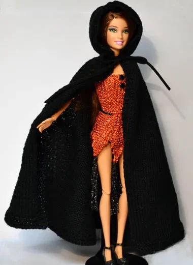 Barbie i långt svart cape med kapuschong över röd paljettklänning.