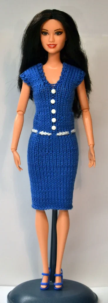 Barbie i blå stickad klänning med vita knappar och vitt skärp.