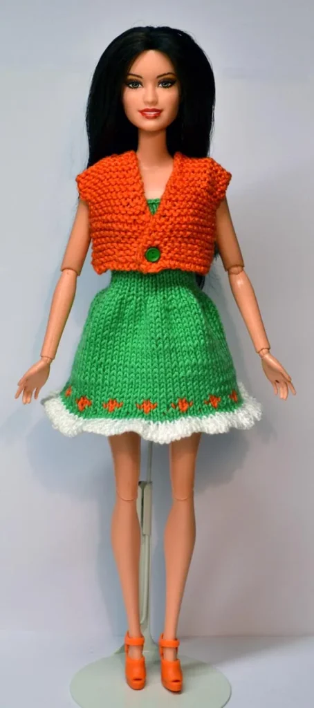 Barbie i grön stickad klänning med orange jacka och vita detaljer.