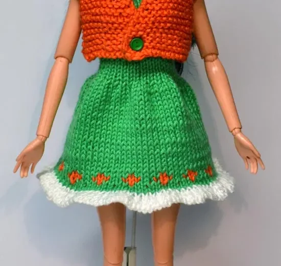 Barbie i grön stickad klänning med orange jacka och vita detaljer.