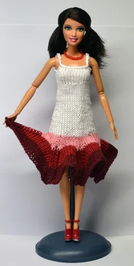 Barbie i vit stickad klänning med röda och rosa ränder nertill.
