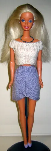 Barbie i lila stickad kjol och vit topp.