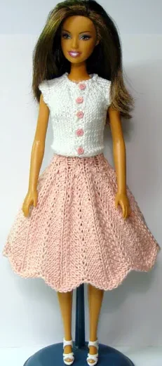 Barbie i rosa stickad kjol med hålmönster och vit topp med rosa knappar.