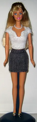 Barbie i vit topp med v-ringning och grå kjol.