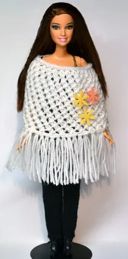 Barbie i vit stickad poncho med fransar och gula blommor.