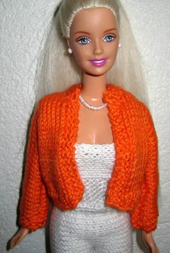 Barbie i orange stickad bolero över vit topp med pärlhalsband.