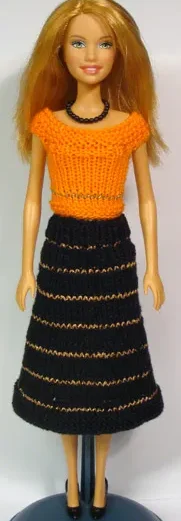 Barbie i svart kjol med guldränder och orange stickad topp.