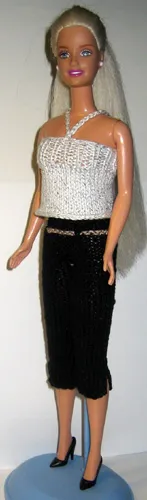 Barbie i vit glittertop och svarta knäbyxor med svarta högklackade skor.