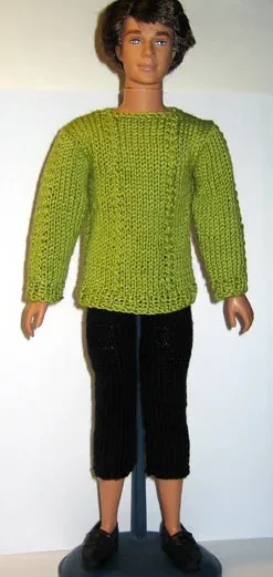 Barbie i grön stickad tröja med flätmönster och svarta byxor.