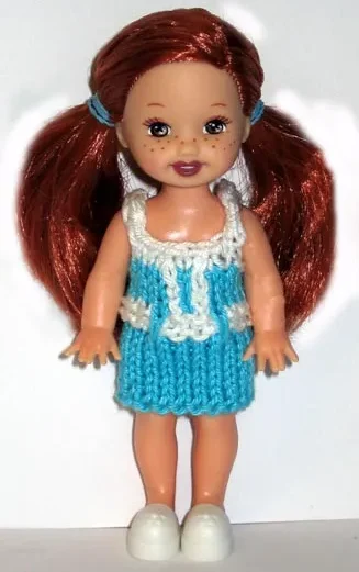 Docka i turkos stickad klänning med vitt skärp och detaljer.