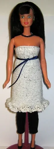 Barbie i vit stickad klänning med blått midjeband och volangkant.