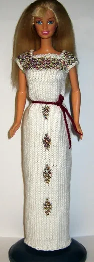 Barbie i vit stickad lång klänning med blommönster och vinrött bälte.