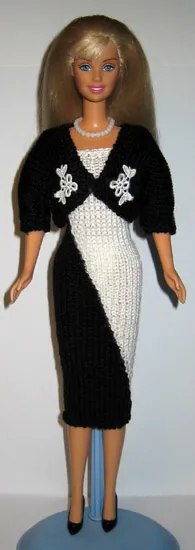 Barbie i svart stickad bolero med vita spetsdetaljer över vit klänning.