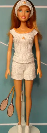 Barbie i vit stickad tennisoutfit med topp och shorts, hållande tennisracket.